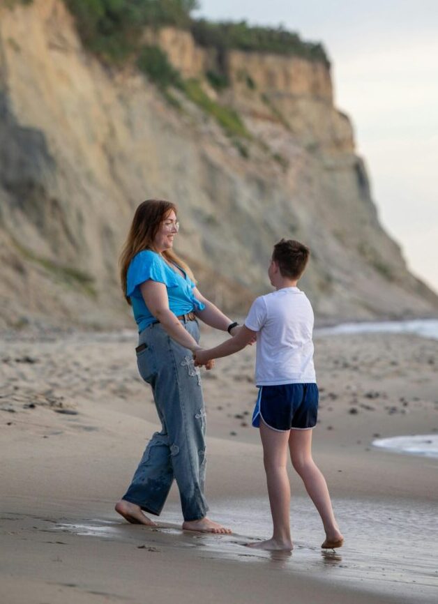 A mother and son bonding during a relaxed walk along a scenic beach with cliffs.